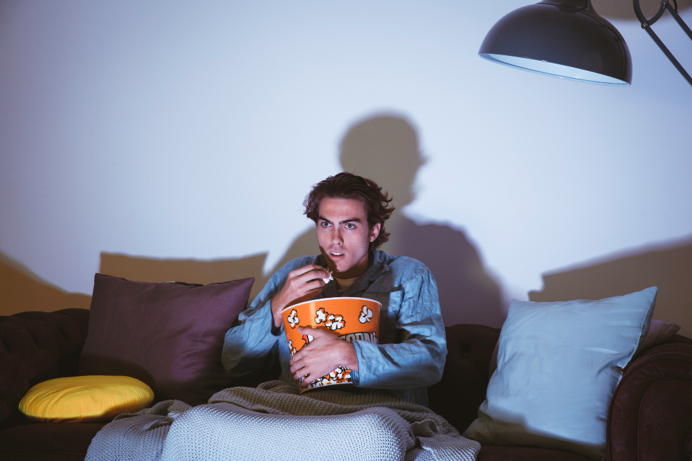 a guy sitting on a couch eating pop corn and watching tv